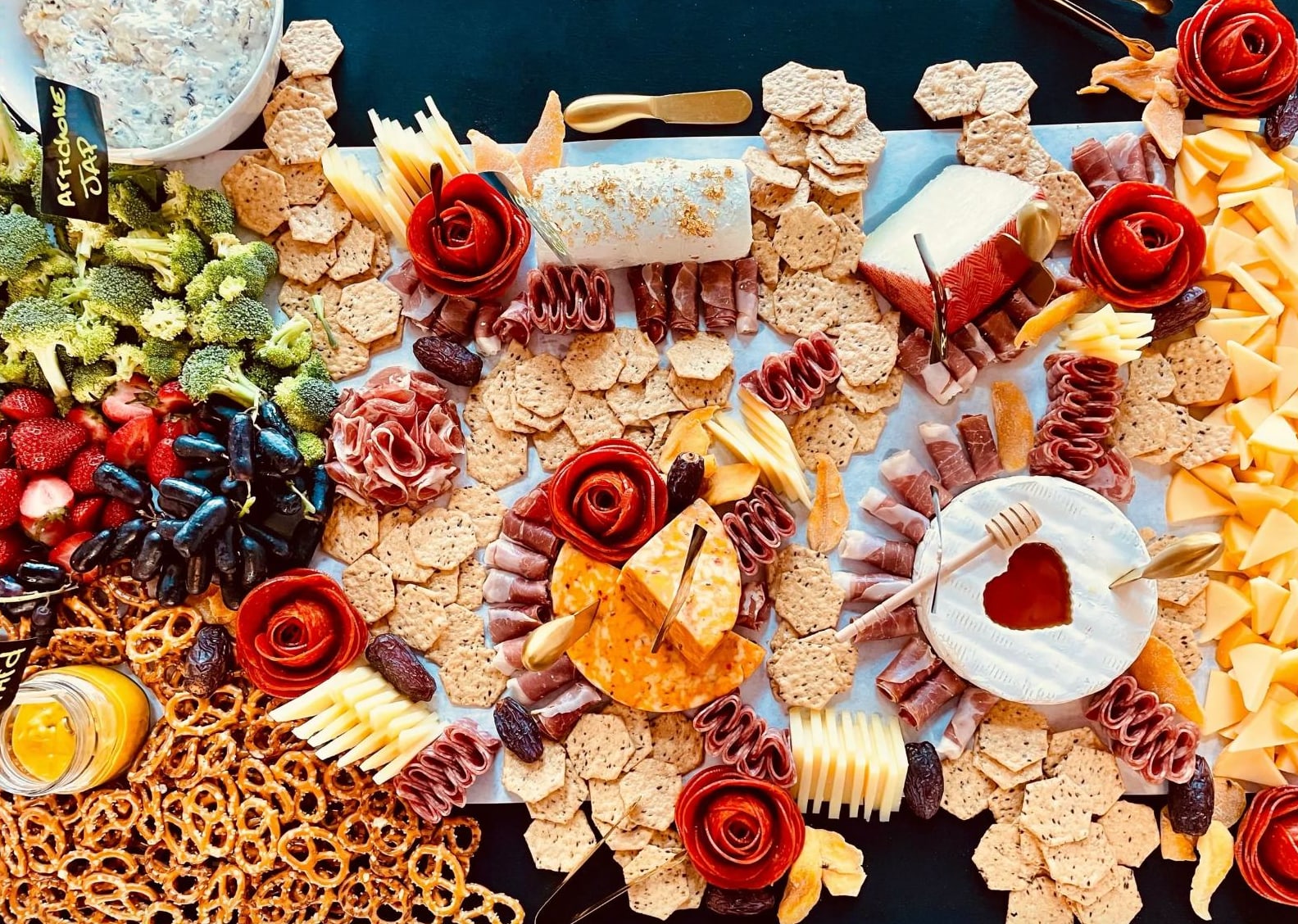An overhead grazing board with salami roses, cheeses, crackers, fruit and pretzels by Rent The Chef